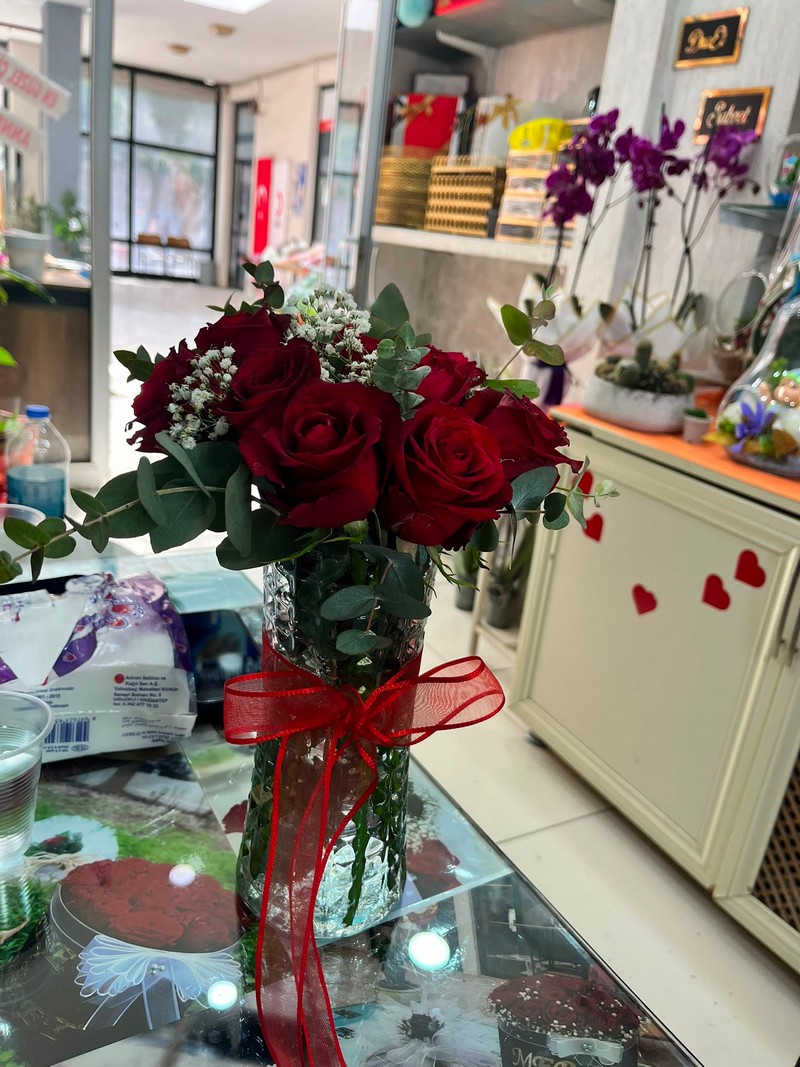 Kırmızı kurdeleli cam vazoda güller ve yeşil yapraklar